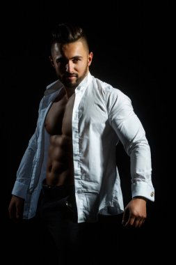 Beyaz gömlekli seksi çıplak vücutlu seksi erkek manken. Siyah stüdyoda düğmeleri iliklenmemiş beyaz gömlekli seksi bir adam. Çıplak gövdesi ve gömleği olan yakışıklı kaslı adam. Açık gömlekli seksi adam.