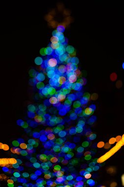 Kar tanesi arka planlı Noel ağacı tatili. Madalyalı Noel Ağacı. Geceleri bulanık Noel ağacı. Işık çelenkleriyle Noel ağacı. İlk yıldız parladı.