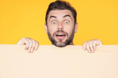 Boş tahtayı tutan ve stüdyo arkaplanını işaret eden yakışıklı, hayret verici adam. Kopyalama alanı olan boş tabela gösteren harika bir adam. Fikir ve teklif. Reklamınız. Boş reklam panosu