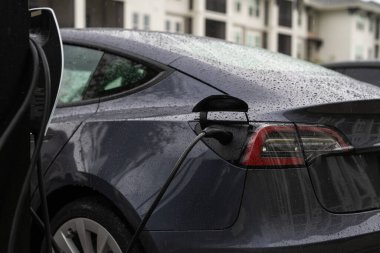 Elektrikli araba şarj oluyor. Benzin istasyonu şarj ediliyor. Yeşil enerjili şarj istasyonu, halka açık otoparkta EV arabalı elektrikli araç. Şarj edilecek güç istasyonu