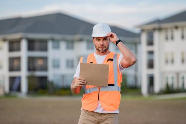 Mühendis kâğıt tahtasını metin için tutuyor. Tabelacı pankart afişi ve poster gösteriyor. İnşaat müdürü ya da mühendis dışarıda kask takıyor. Erkek inşaat mühendisi