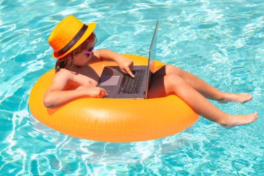 Yaz işleri ve online teknoloji. Uzaktan kumandalı çocuk bilardoda çalışıyor. Küçük iş adamı yazın havuz suyunda dizüstü bilgisayarda çalışıyor.