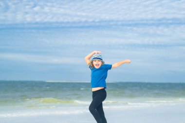 Komik çocuk yaz plajında dışarıda oynuyor. Yaz tatiline çıkmış duygusal bir çocuk. Mutlu çocuk mavi gökyüzüne ve denize karşı dinleniyor. Yaz tatili kavramı. Çocuklar yaz seyahati ve macera