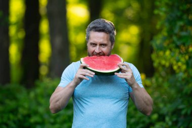 Karpuzlu erkek yüzü, yaklaş. Yazlık parkta karpuz yiyen komik bir adam. Karpuz yiyen bir adam. 40 'ların adamı dışarıda meyve yiyor. Karpuz seven bir adam