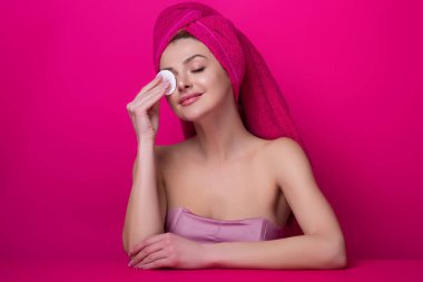 Pamuk yastıklı güzel bir kadın, yüzüne losyon sürüyor, makyajı kaldırıyor. Cilt bakımı. Pamukla yüzünü temizleyen bir kızın stüdyo portresi, izole bir arka plan. Yüz toneri ve pamuk pedi