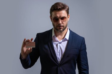 Kredi kartı konsepti. Beyaz ırkın başarılı 40 'lı yılların iş adamı, bankacılık kartını gri arka planda, stüdyo portresi üzerinde izole bir şekilde tutuyor. İnsanların yaşam tarzı konsepti. Satın alma ve geri ödeme ödülleri