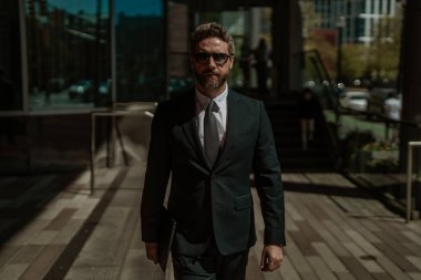 Modern ofis binasının önünde başarılı bir iş adamı duruyor. İş başarısı. Dışarıyı düşünen bir iş adamı. Takım elbiseli modern iş adamı ofis manzarasının yanında duruyor.