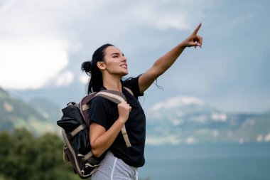 İsviçre Alpleri 'ndeki dağ gölünde sırt çantalı bir kadın turist. Macera, seyahat, turizm ve yürüyüş insanları konsepti. Parmakla işaret eden turist kız. Yürüyüşçü kadın