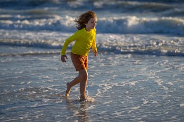 Mutlu çocuk yaz denizinde su sıçratarak oynuyor. Yaz tatili. Çocuk denizde dalgalarla oynuyor. Küçük çocuk denizde oynuyor ve su damlaları sıçrıyor. Çocuk denizde su sıçratmaca oynuyor. Yaz tatili