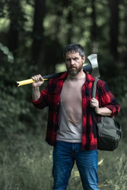 Olgun Oduncu 'nun ciddi suratı ormanda balta tutuyor. Baltalı bir oduncu kesmeden önce ağacı inceler. Ciddi bir oduncu. Millennial orta yaşlı adam elinde büyük bir balta tutuyor.