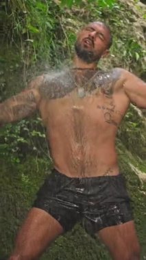 Naked sexy man at a tropical waterfall. Man relaxing in water with freedom. Strong fit Man in waterfall in tropical nature. Wellness spa concept in nature. Wild nature. Muscular Hispanic man posing.