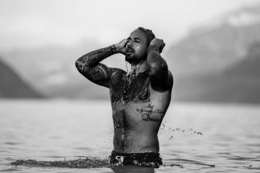 Adam gölde rahatladı. Yaz plajında çıplak gövdeli yakışıklı bir adam. Alps gölündeki seksi bir adamın portresi. Özgürlük ve seyahat macerası. Seksi gezgin İsviçre 'de manzaranın tadını çıkarıyor