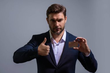 Gri arka planda kredi kartı tutan bir iş adamı. İspanyol adam kredi kartını gösteriyor. Kredi kartı ya da banka kartı. İnternetten alışveriş konsepti. İndirim teklifi, online alışveriş.