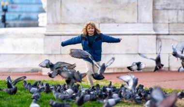 Child feeding and chasing birds on autumn day. Child run for pigeons on the street outdoor. A child chases pigeons in a park. Child playing with doves in the city. Kid Little girl running, flaunts the clipart