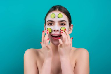 Salatalık maskesi. Cilt bakımı. Mavi stüdyo arka planında yüz kremi süren bir kadın. Genç spa modeli yüz bakımı kremi kullanıyor. Yüz kremi, nemlendirici, besleyici krem