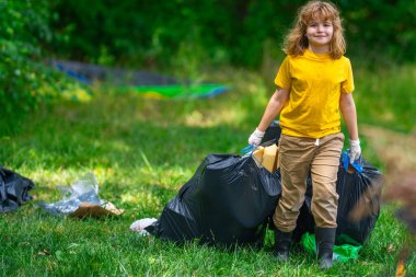 Çevre plastik kirliliği. Ormanda çöp toplayan ve elinde çöp torbası tutan gönüllü bir çocuk. Çevresel koruma. Çevre aktivisti. Çevre koruma ve atık kirliliği