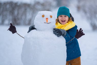 Çocuk kışın kardan adam için kartopu yapıyor. Çocuk karda oynuyor. Açık havada aktif kış oyunları. Çocuk karla oynarken eğleniyor. Çocuklar için açık havada kış tatili. Güneşli kış gününde çocuk oyunu