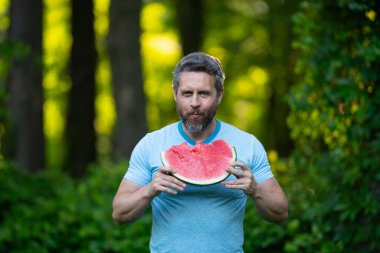 Karpuzlu komik erkek suratı, yaklaş. Yazlık parkta karpuz yiyen mutlu bir adam. Karpuz yiyen bir adam. 40 'ların adamı dışarıda meyve yiyor. Karpuz seven bir adam