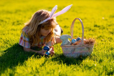 Paskalya çocuğu parkta. Paskalya yumurtası avlayan çocuk. Tavşan kulaklı şirin çocuk parkta paskalya geçiriyor. Çocuklar paskalya yumurtası avlar.