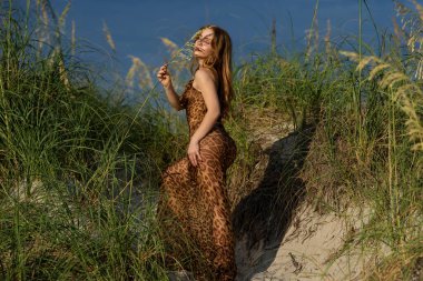 Moda elbiseli moda kadını. Yaz Vogue 'u. Çekici kadın sahada dikilirken elbise giyer. Kız şehvetli ve seksi görünüyor. Moda Yaşam Tarzı. Dışarıda Güzel Genç Bir Kadının Moda Portresi