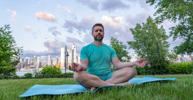 Latin Adam dışarıda otların içinde meditasyon yapıyor. Sporcu şehir parkında yoga yaparken asana meditasyonu yapıyor. Atletik erkek meditasyonu, rahatlama, sağlıklı yaşam tarzı kavramı. Açık havada meditasyon.