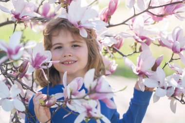 Çocuklar için bahar eğlencesi. Çocuk güzel bir bahar bahçesinde dışarıda oynuyor. Çiçekli çocuk yüzü. Güzel bir bahar gününde kiraz bahçesinde küçük sevimli bir çocuk. Bahar çiçekleri arasında mutlu bir çocuk