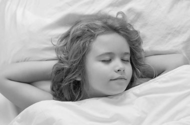 Çocuk yatakta uyuyor. Battaniyenin altında uyuyan tatlı çocuk. Çocuk yastığa uzanmış. Çocuk uyuyor, sağlıklı bir uyku çekiyor ya da kestiriyor.