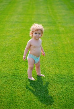 Güneşli yaz akşamında yeşil çimlerde çıplak ayakla yürüyen bebek.
