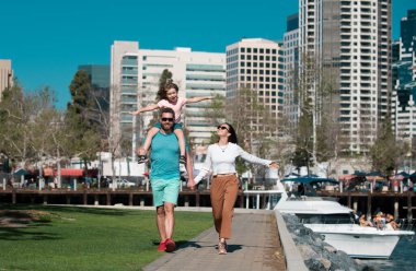 Happy family walking the city street, casual lifestyle. Summer vacation. Mother, father and kids on vacation on background of skyscrapers in San Diego. Father giving son ride on back outside