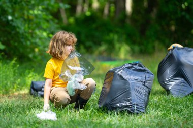 Lastik eldivenli çocuk çöp torbasıyla ormandaki çöpleri temizliyor. Eko, çevre koruma. Kirliliği geri dönüştür. Çocuk çöp ve plastik çöp topluyor. Çevreyi koru. Eko çocuklar