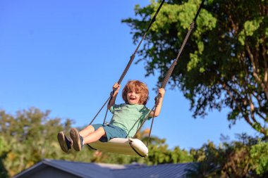 Salıncakta sallanan çocuk. Çocuk parkta sallanıyor. Sevimli, heyecanlı, şaşkın çocuk salıncakta. Salıncakta sallanan sevimli çocuk. Çılgın oyuncu çocuk çok yüksekte sallanıyor