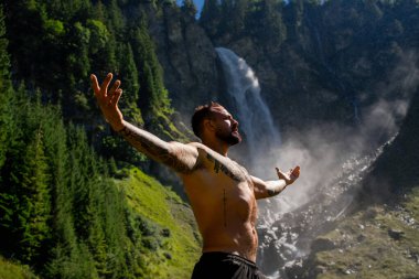 Yaz tatilindeki erkek turist. Yaz tatilinde çıplak gövdeli yakışıklı bir adam. Dışarıda seksi bir yürüyüşçü var. Şelale manzarasında yürüyen bir turist. İnsan Seyahati ve doğa