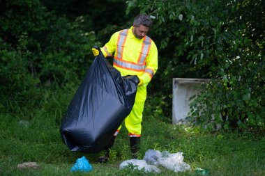 Çevre plastik kirliliği. Ormanda çöp toplayan ve elinde çöp torbası tutan bir gönüllü. Çevresel koruma. Çevre aktivisti. Çevre koruma ve atık kirliliği