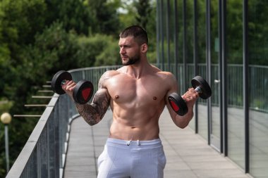 Kas yığını adam spor salonunda dambıllarla antrenman yapıyor. Spor salonunda poz veren kaslı yakışıklı bir adam. Kas sporcusu dambılı kaldırıyor. Spor kulübünde esneme, spor egzersizleri.