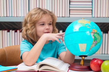 School pupil looking at globe in library, geography lesson. School child studying in classroom at elementary school. Kid studying on lesson in class at elementary school