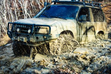 Bir araba çamur püskürtür. Çamurda yuvarlan. Off-road aracı dağ yolunda gidiyor. Vahşi dağlarda off-road. Kirli araba aynası kapısı, cam kapağı ve arabanın üzerindeki çamur deseninin yakın plan fotoğraf çekimi.