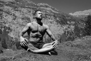 Latin Adam dışarıda otların içinde meditasyon yapıyor. Sporcu şehir parkında yoga yaparken asana meditasyonu yapıyor. Atletik erkek meditasyonu, rahatlama, sağlıklı yaşam tarzı kavramı. Açık havada meditasyon.