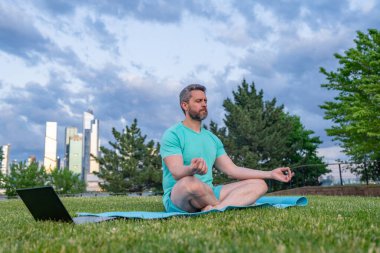 Sport Man dışarıda çimenlerde nilüferde meditasyon yapıyor. Sporcu şehir parkında yoga yaparken asana meditasyonu yapıyor. Atletik erkek meditasyonu, rahatlama, sağlıklı yaşam tarzı kavramı. Açık havada meditasyon.