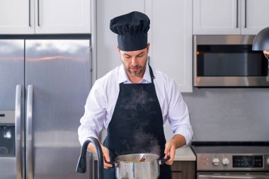 Adam mutfakta yemek pişiriyor. Şef aşçı tencereli bir yemek hazırlıyor. Menü tarifi sağlıklı yemek. Evde yemek pişiren adam mutfakta yemek hazırlıyor. Olgun bir adam mutfakta yemek hazırlıyor.