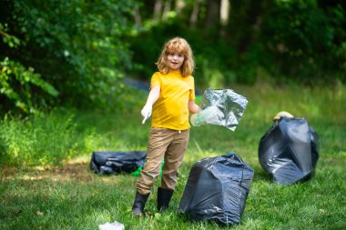 Lastik eldivenli çocuk çöp torbasıyla ormandaki çöpleri temizliyor. Eko, çevre koruma. Kirliliği geri dönüştür. Çocuk çöp ve plastik çöp topluyor. Çevreyi koru. Eko çocuklar