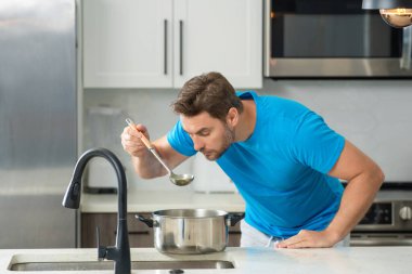 Evde yemek pişirmek. Mutfakta yemek hazırlayan adam. Erkek aşçı evde yemek hazırlıyor. Şef yemek yapıyor. Yemek pişiren adam, mutfak tenceresi, yemek tabağı. Adam mutfak içinde çorba hazırlıyor.