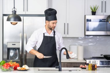 Modern mutfakta yemek pişiren çekici bir adam. Evde yemek pişiren yakışıklı adam mutfakta salata hazırlıyor. Modern mutfakta yemek hazırlayan sıradan bir adam. Olgun bir adam mutfak masasında yemek hazırlıyor.