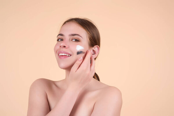 Beautiful model applying cosmetic cream treatment on face. Facial treatment. Beauty portrait of young topless woman with bare shoulders applying face cream