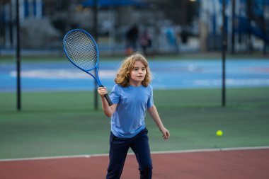 Çocuk tenis oynuyor. Küçük çocuk tenis raketiyle tenis topuna vurdu. Çocuklar için aktif egzersiz. Çocuklar için yaz etkinlikleri. Çocuk tenis oynamayı öğreniyor. Sport Kid sahada topa vuruyor.