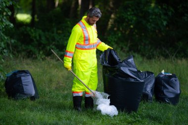 Gönüllü adam çöpleri topluyor, doğadaki atıkları topluyor. Toprak kirliliği, çevresel sorunlar. Plastik çöp yığını doldur. Doğanın kirliliği. Ekoloji konsepti. Çevre kirliliği