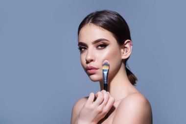 Beautiful woman applying makeup holding brush. Beauty make up concept of an young woman. Beauty salon. Skin care and natural makeup. Girl gets blush on the cheekbones. Beauty care and treatment