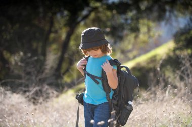 Sırt çantalı küçük bir çocuk manzaralı dağlarda yürüyüş yapıyor. Çocuk yerel bir turist yerel bir yürüyüşe çıkıyor.