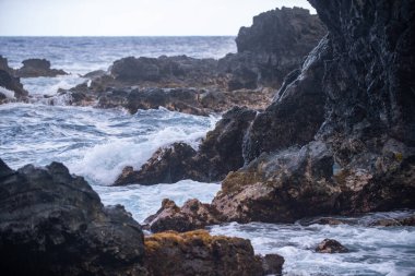Atlantik okyanus dalgaları tarafından yenilmiş soğuk siyah lav. Sahildeki kayalara vuran deniz dalgalarının görüntüsü. Dalgalar ve kayalar