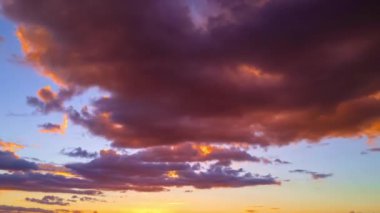 Bulutların üzerinde dramatik bir ışıkla gün batımı. Güneş batıyor, bulutlar mavi ve turuncu dramatik gökyüzünde, güneş ışınlarıyla. Gece Gökyüzü zaman çizelgesi. Gün batımında hareket eden bulutlar. Akşam Bulutları