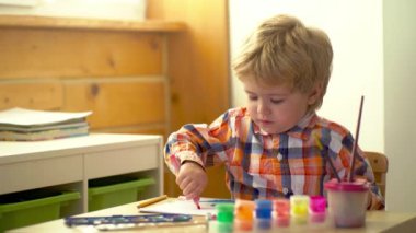 Küçük şirin bir çocuk resmi ve çizimi. Pastel boyalı ve kağıda çizim yapan bir çocuk. Yaratıcı düşünce ve çocukların sanatsal kavramları. Boya fırçası ve suluboya ile çocuk resmi. Bebek resmi
